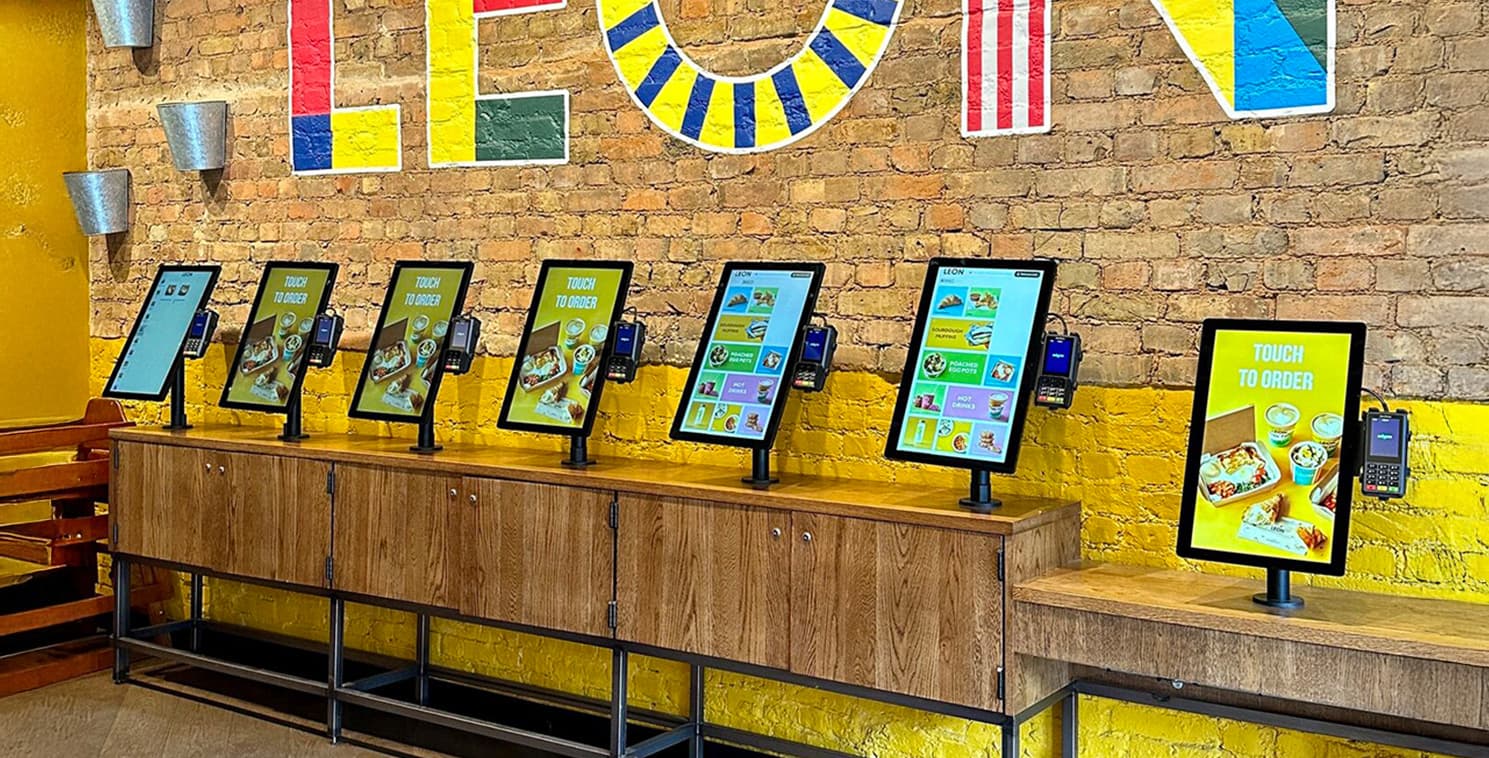 Multiple Elo touchscreen self-order kiosks line a restaurant counter, each equipped with a payment device and menu interface for fast, efficient self-ordering.